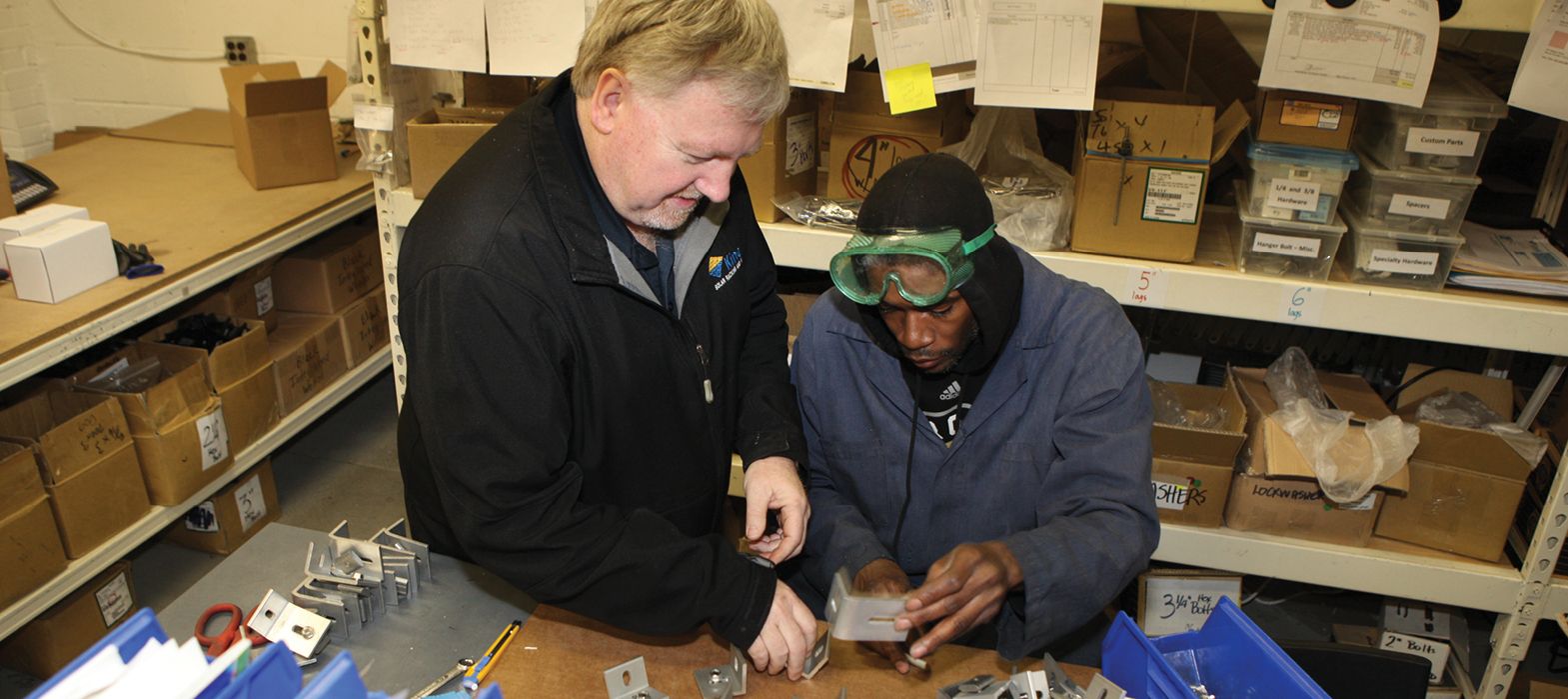 middle aged man demonstrating how to use tools to a younger man