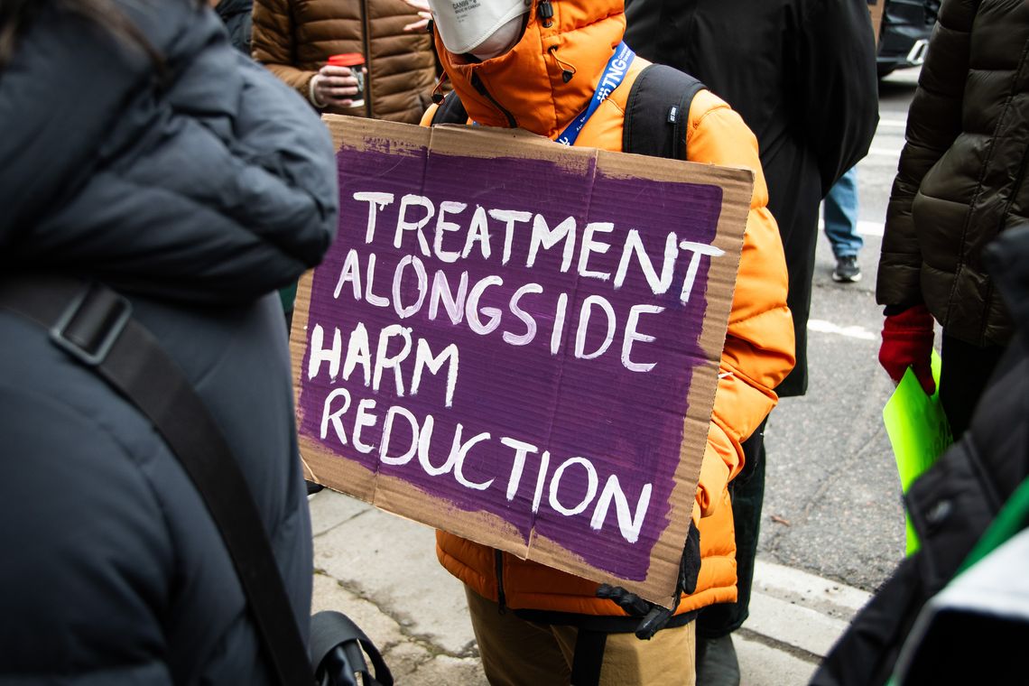 person holding sign "Treatment alongside Harm Reduction"