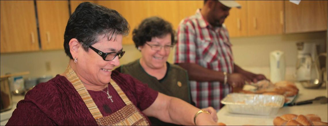 two women and a man preparing food in a kitchen