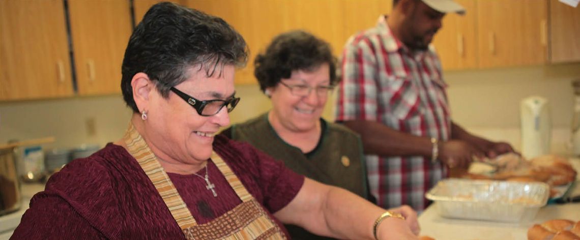 two women and a man preparing food in a kitchen