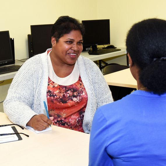 smiling women in a computer classroom talking to an instructor