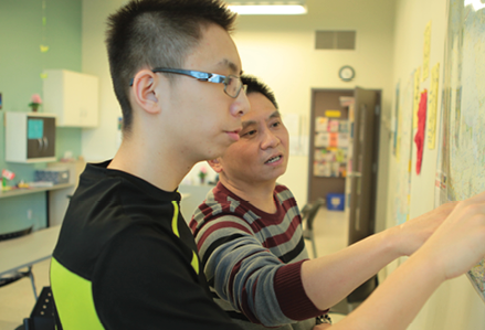 teenaged boy and his father pointing at a chalkboard