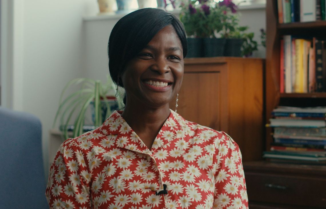 smiling woman sitting beside a bookshelf