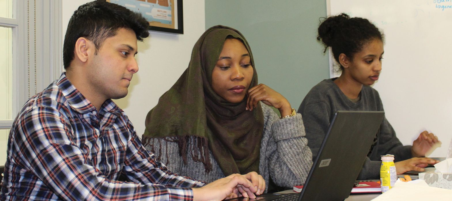 three young people sitting at a desk working