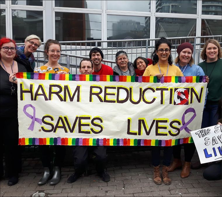 people holding sign that reads "Harm reduction saves lives"